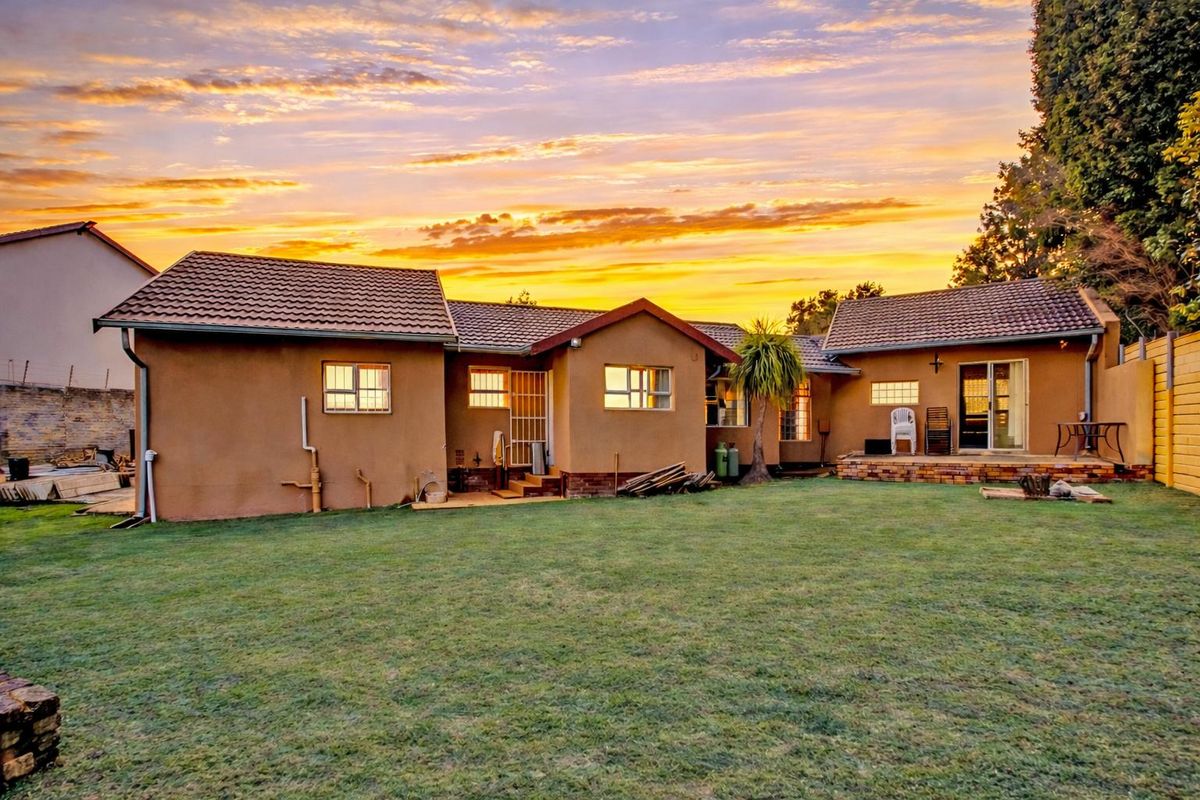 Rear view of the house featuring a tiled roof, brick patio area, and a spacious garden at sunset.