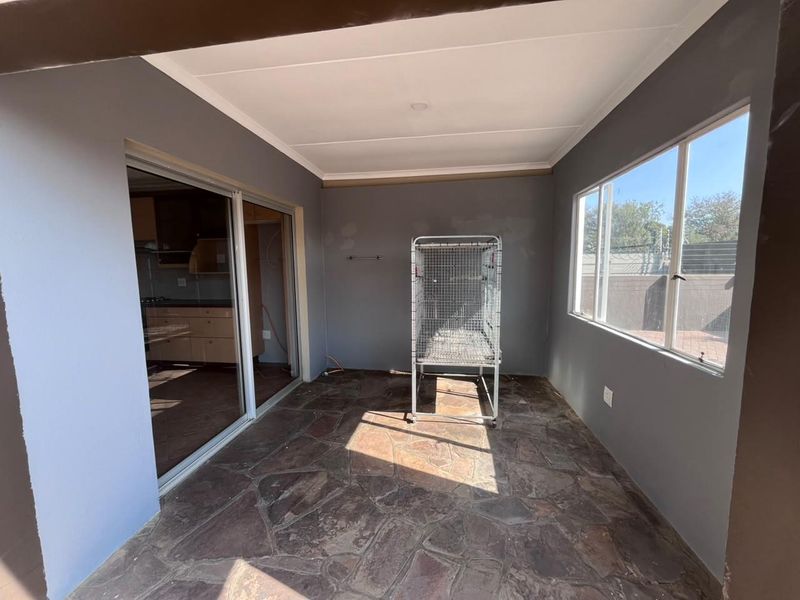A covered patio area featuring natural stone flooring, large windows, and sliding door access to the kitchen, currently presented as an empty space.