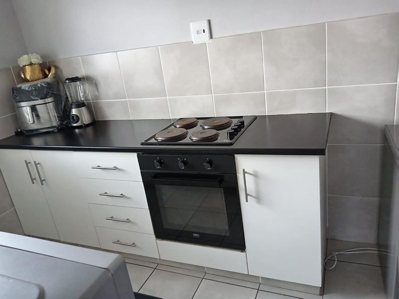 A functional kitchen area featuring white cabinetry, a black laminate countertop, a built-in oven with an electric hob, and neutral tiled splashbacks.