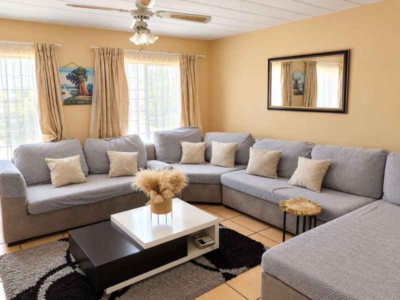 A comfortable living room featuring tiled flooring, a ceiling fan, and large windows with security bars, providing a functional and well-lit space.