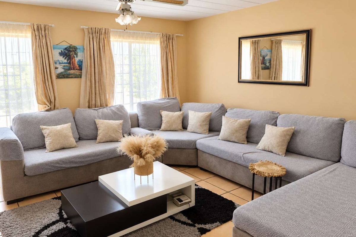 A comfortable living room featuring tiled flooring, a ceiling fan, and large windows with security bars, providing a functional and well-lit space.