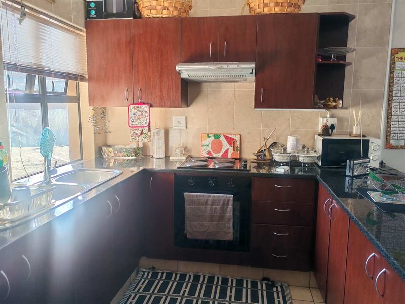 A functional kitchen featuring dark wood cabinetry, granite countertops, a built-in oven with hob, and a stainless steel double sink.