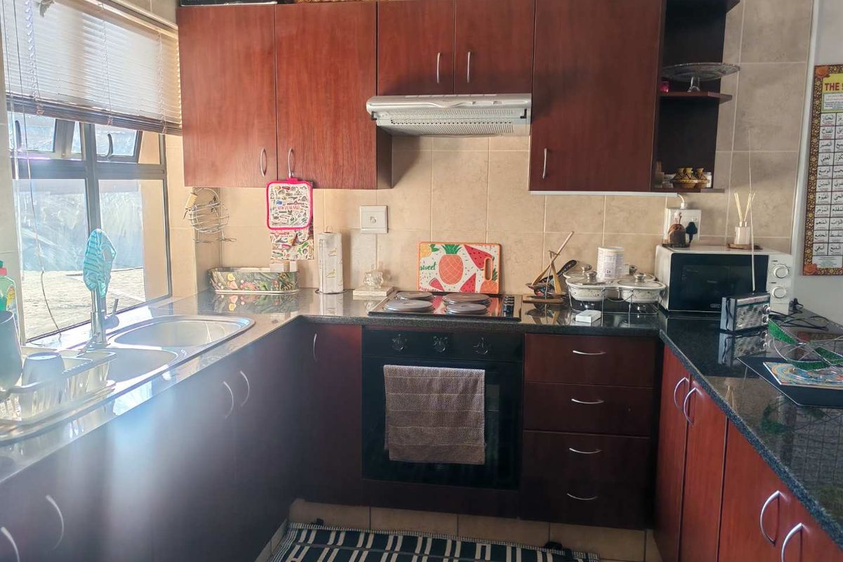 A functional kitchen featuring dark wood cabinetry, granite countertops, a built-in oven with hob, and a stainless steel double sink.