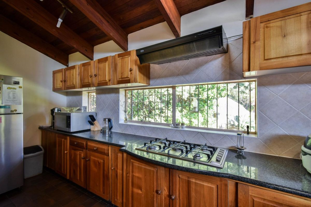 A functional kitchen featuring wooden cabinetry, granite countertops, a built-in gas hob, and an extractor fan under a vaulted timber ceiling.
