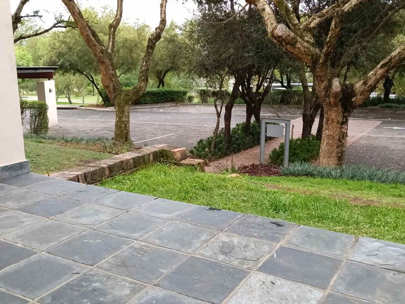 A ground-level patio featuring slate tile flooring, overlooking a landscaped garden area and communal parking space.