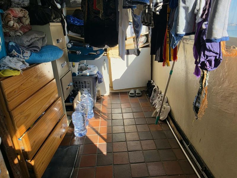 A narrow balcony area featuring tiled flooring, currently utilized for storage and laundry drying.