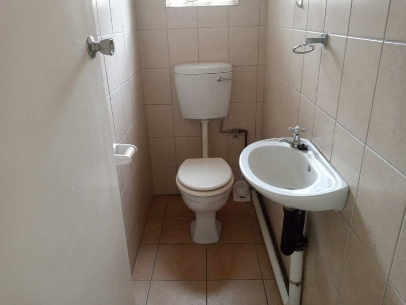 A compact, functional bathroom featuring a wall-mounted basin, standard toilet, and full-height ceramic wall tiling.