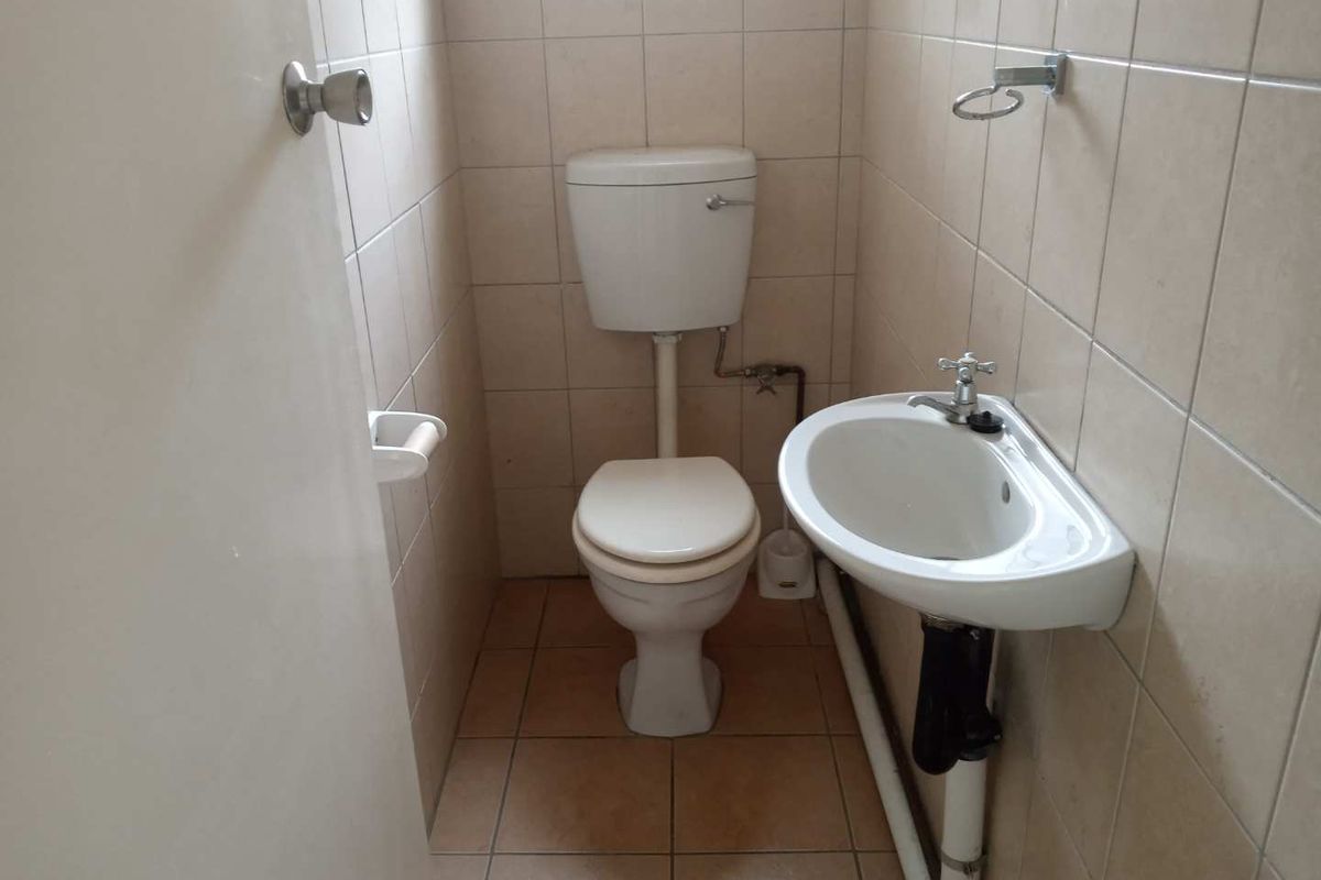 A compact, functional bathroom featuring a wall-mounted basin, standard toilet, and full-height ceramic wall tiling.