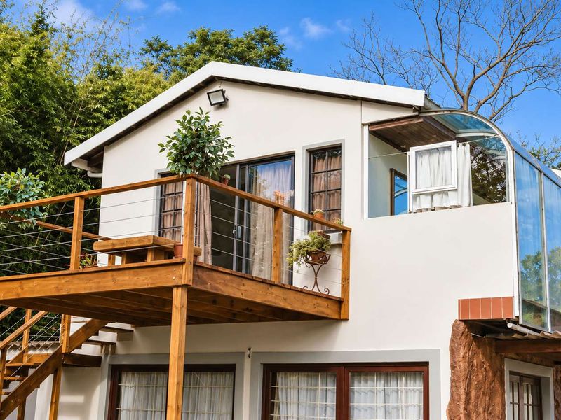Rear view of the property featuring a raised wooden balcony, external staircase, and a modern glass-enclosed sunroom extension.