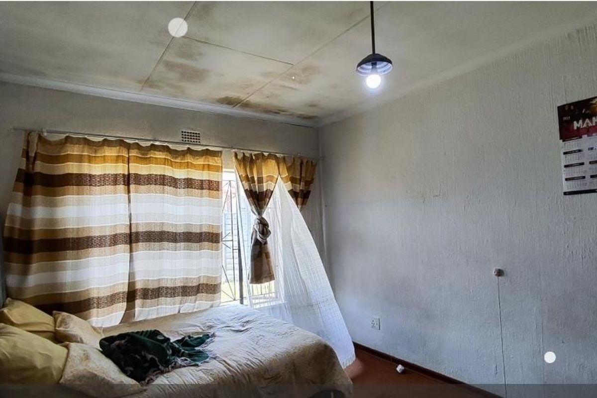A bedroom featuring a window with security bars and a ceiling showing significant signs of water damage and staining.