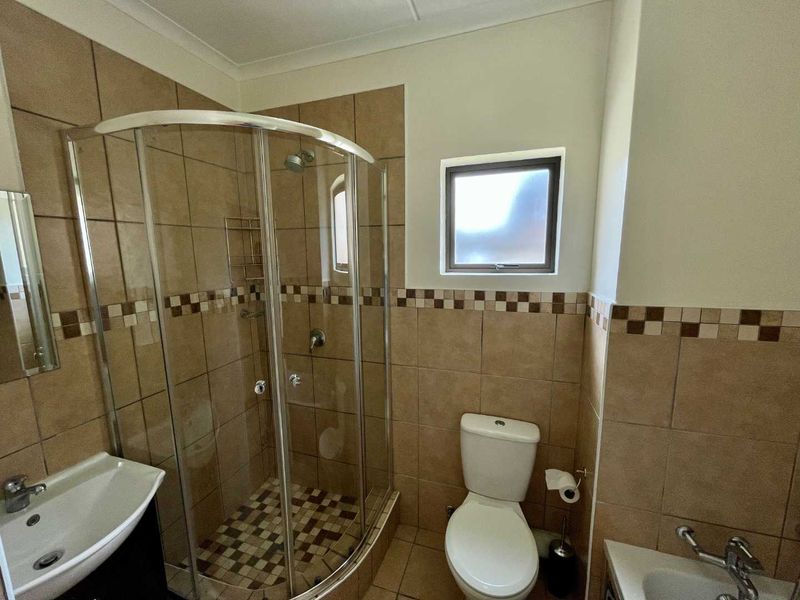A functional bathroom featuring a curved glass shower enclosure, pedestal basin, and neutral ceramic tiling throughout.