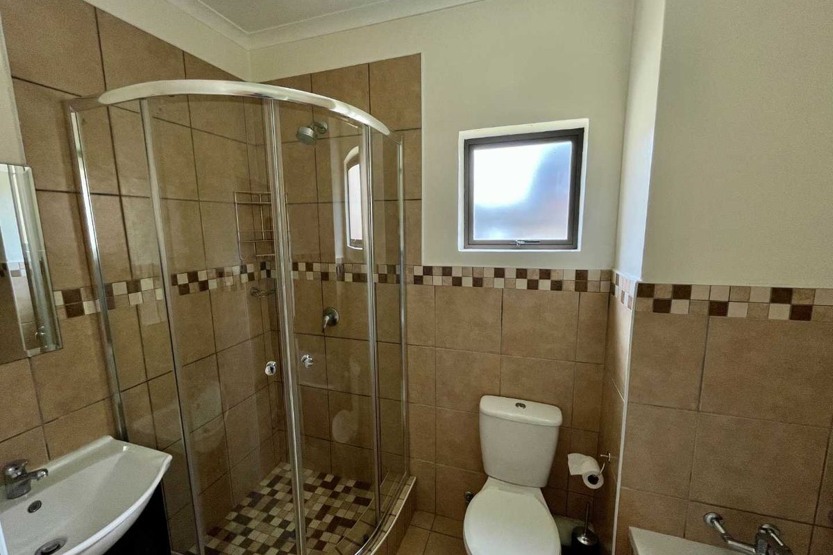 A functional bathroom featuring a curved glass shower enclosure, pedestal basin, and neutral ceramic tiling throughout.