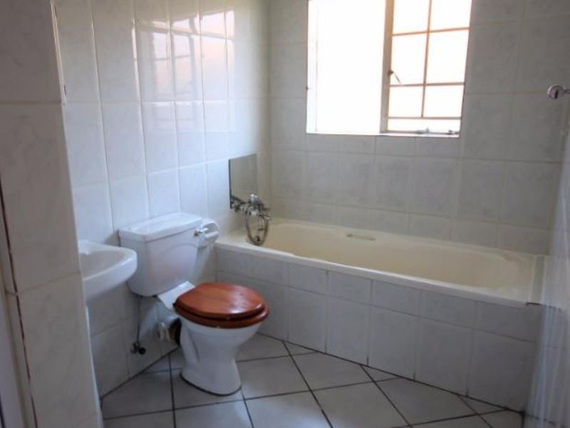 A functional bathroom featuring a bathtub, pedestal basin, and toilet with neutral tiled finishes throughout.