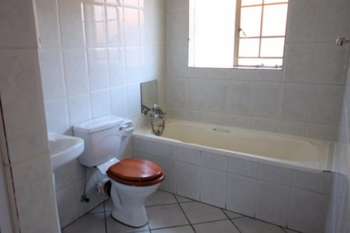 A functional bathroom featuring a bathtub, pedestal basin, and toilet with neutral tiled finishes throughout.