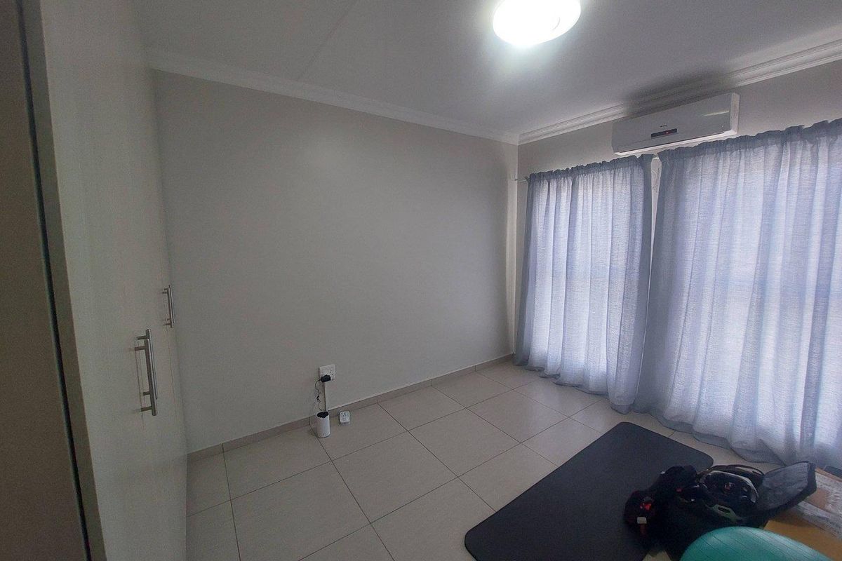 A bright bedroom featuring tiled flooring, built-in cupboards, and a wall-mounted air conditioning unit.