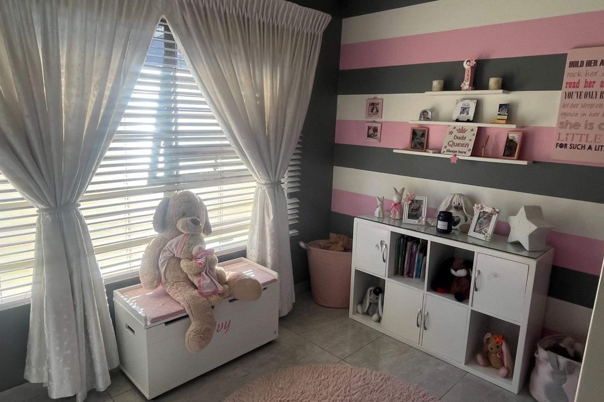 A bedroom featuring tiled flooring, venetian blinds, and built-in shelving, currently styled as a child's room with decorative wall finishes.