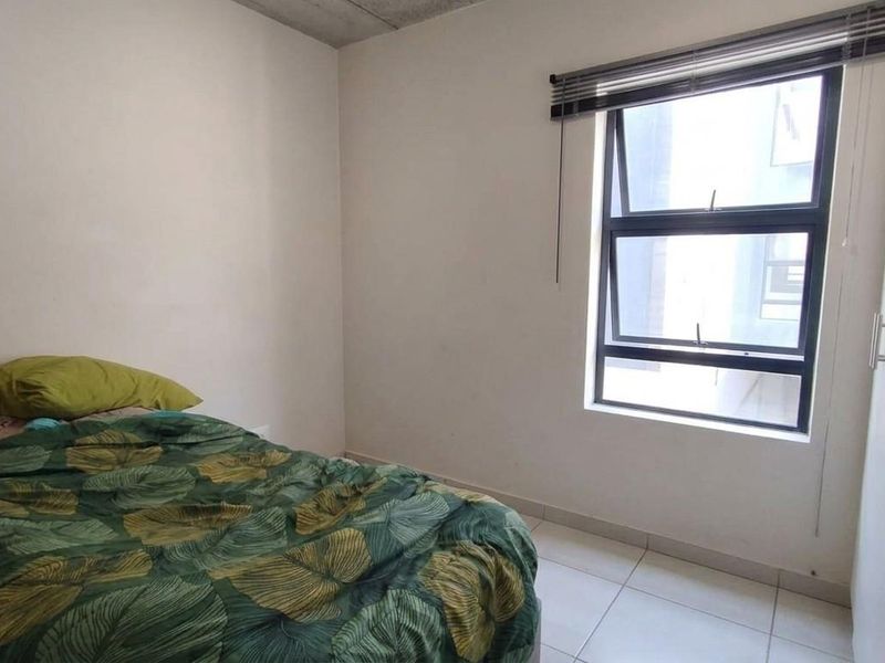 A functional bedroom featuring tiled flooring, a built-in wardrobe, and an aluminium window with a venetian blind.