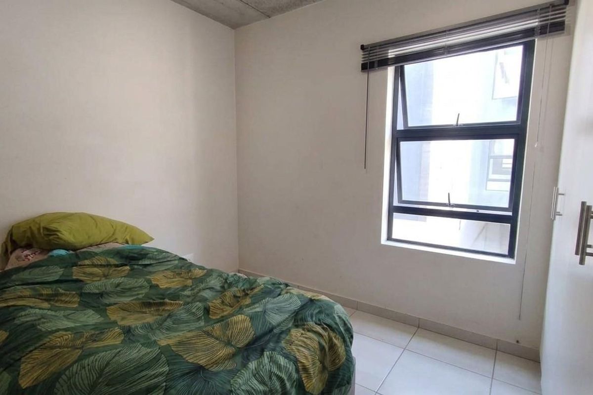 A functional bedroom featuring tiled flooring, a built-in wardrobe, and an aluminium window with a venetian blind.