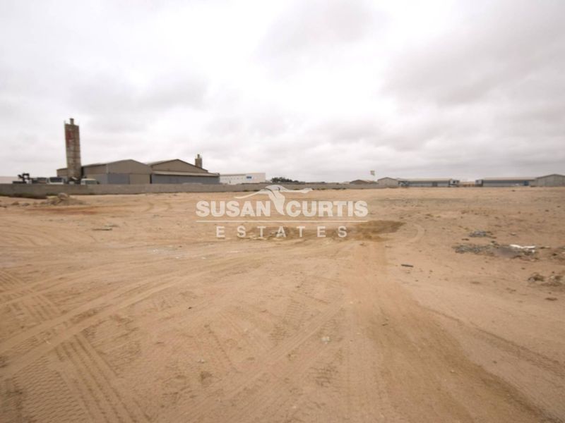 A wide-angle view of a vacant commercial land plot featuring a perimeter wall and street lighting, suitable for industrial or commercial development.