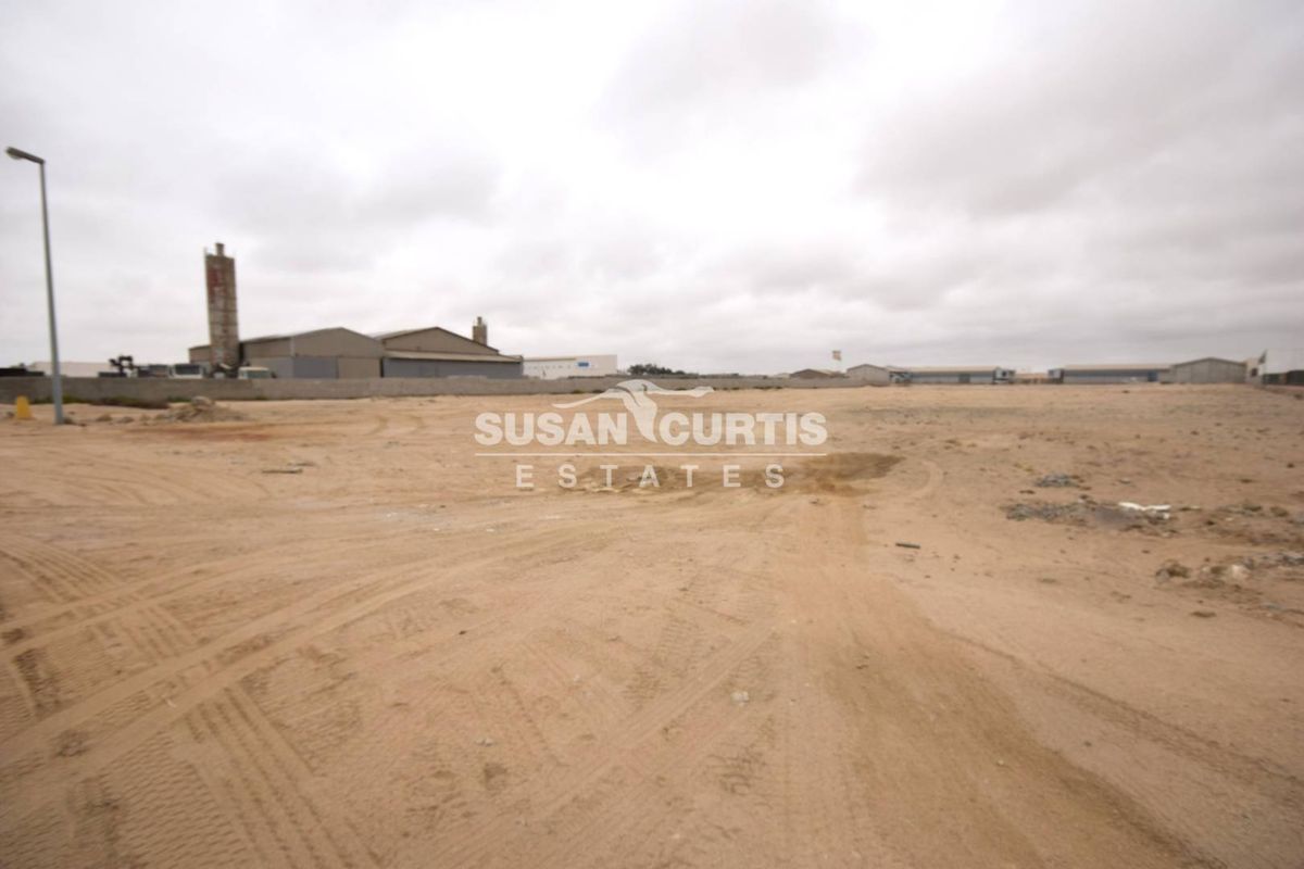 A wide-angle view of a vacant commercial land plot featuring a perimeter wall and street lighting, suitable for industrial or commercial development.