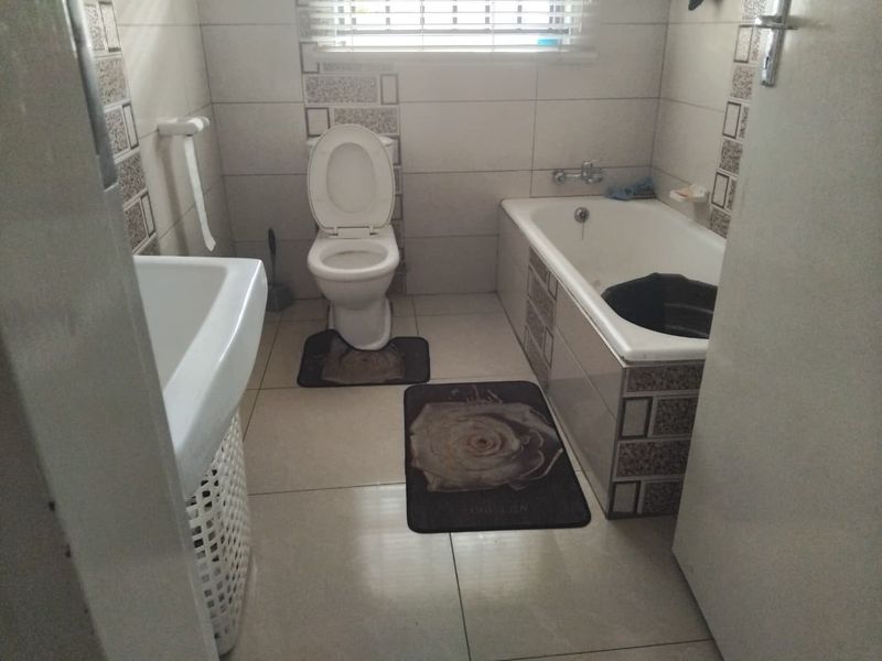 A functional bathroom featuring a bathtub, pedestal basin, and toilet with tiled walls and flooring.