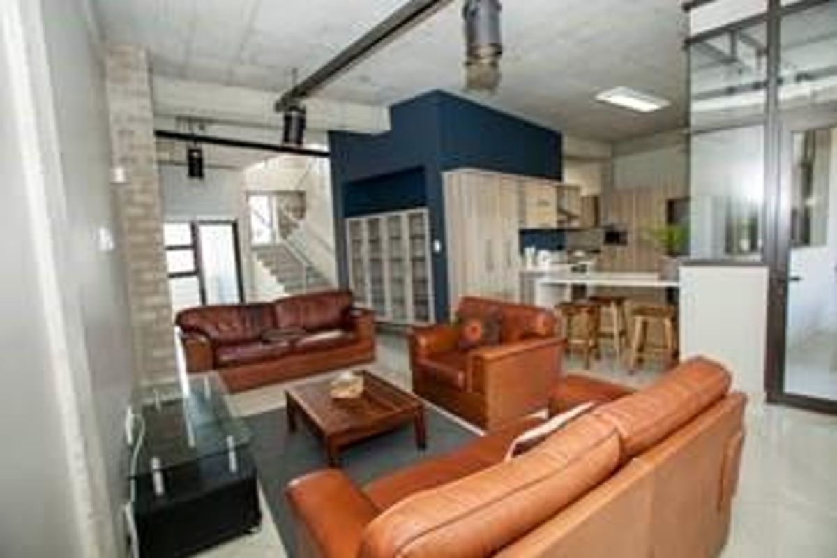 Spacious open-plan office area featuring an industrial aesthetic with exposed concrete ceilings, modern built-in cabinetry, and a glass-partitioned meeting space.