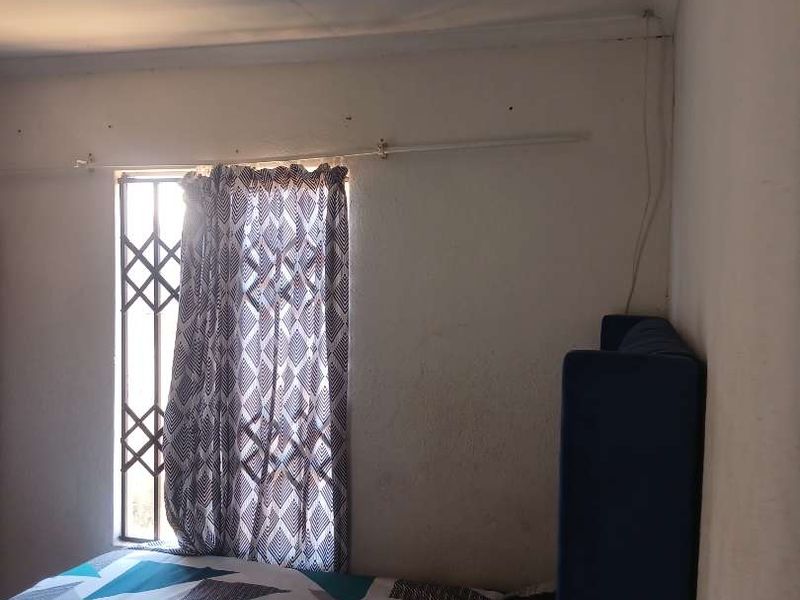 A bedroom featuring a window with a security gate and curtain rail, showing signs of wear on the ceiling and walls.