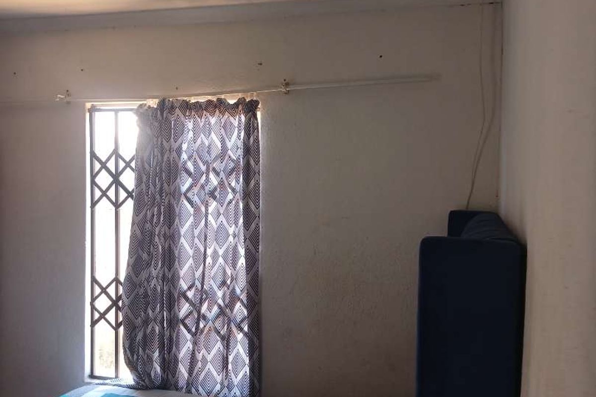 A bedroom featuring a window with a security gate and curtain rail, showing signs of wear on the ceiling and walls.