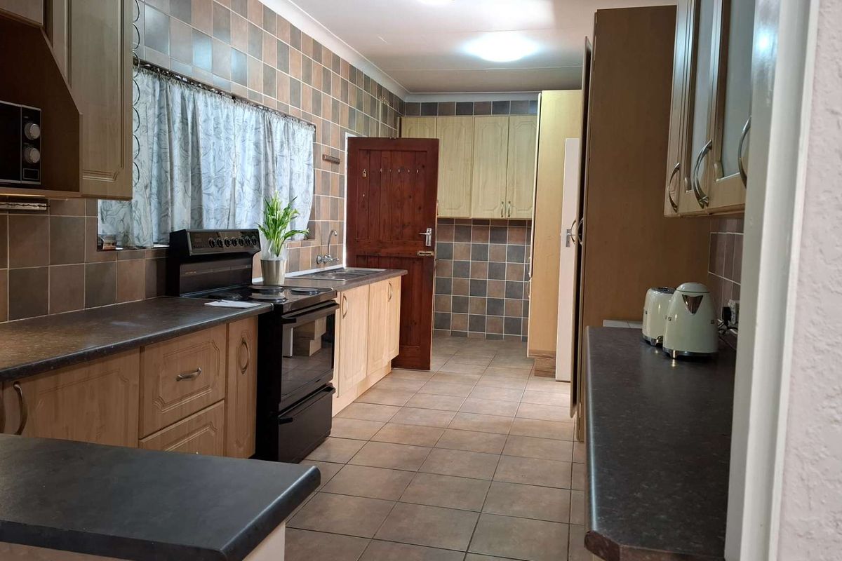 A functional kitchen featuring laminate cabinetry, tiled splashbacks, and tiled flooring, offering a dated aesthetic with potential for modern renovation.