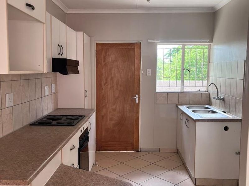 A functional kitchen featuring built-in cabinetry, laminate countertops, an electric hob, oven, and a double basin sink with tiled splashbacks and flooring.