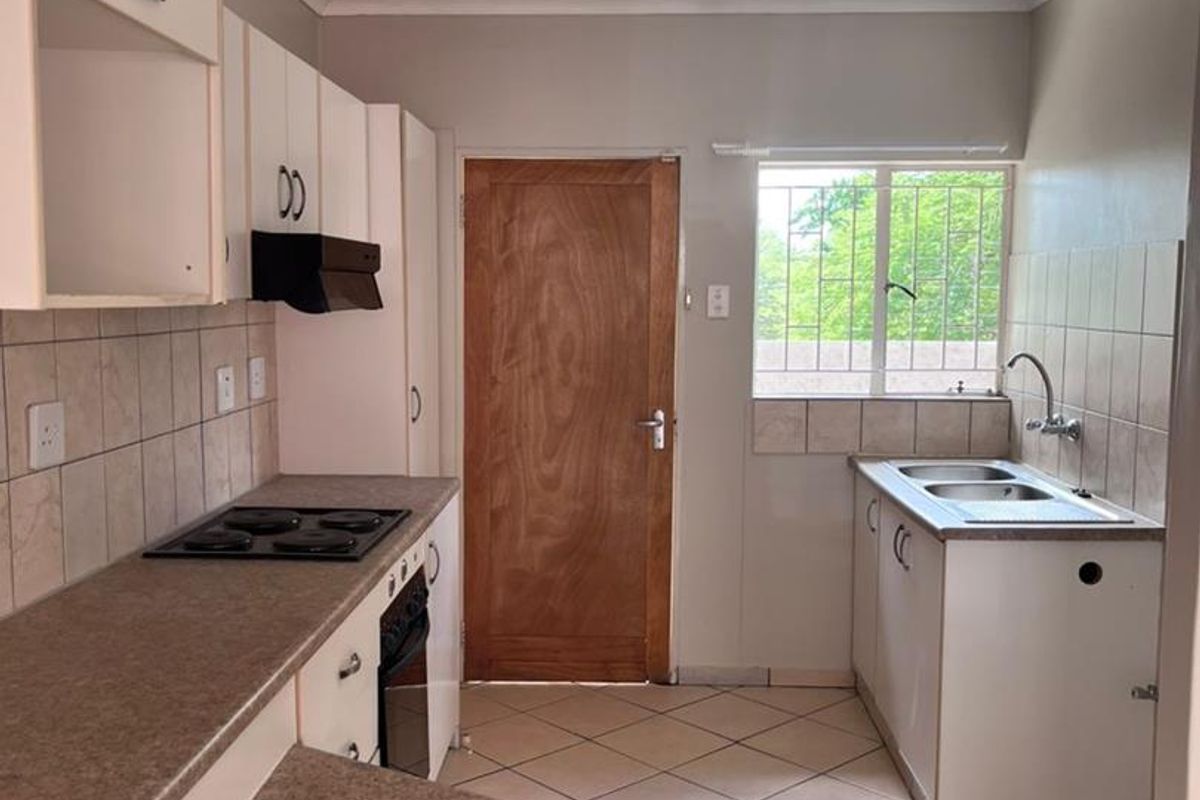 A functional kitchen featuring built-in cabinetry, laminate countertops, an electric hob, oven, and a double basin sink with tiled splashbacks and flooring.