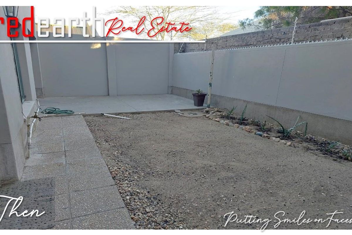 A rear courtyard area featuring a concrete patio section and an unfinished garden space enclosed by high perimeter boundary walls.