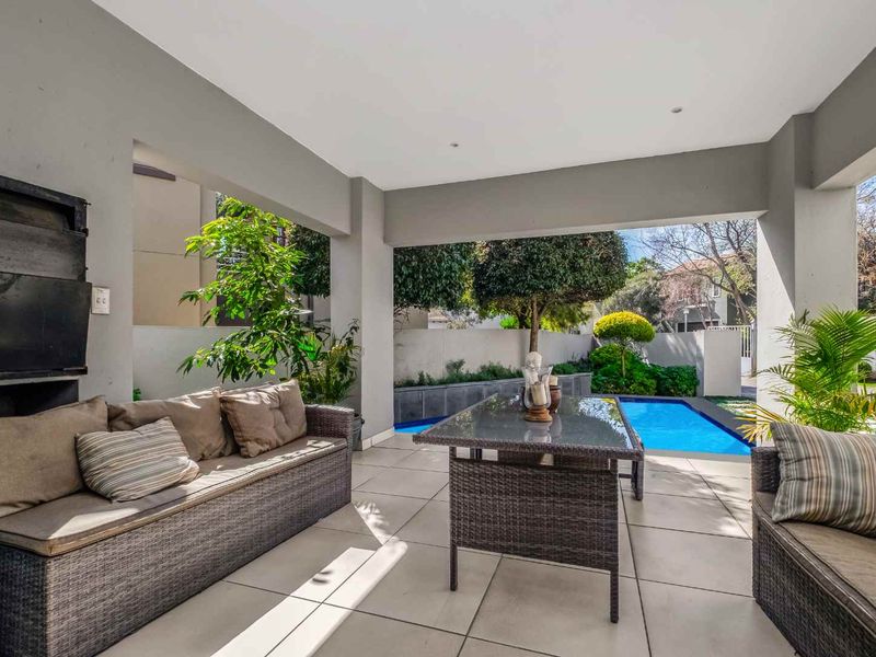 Covered outdoor patio featuring a built-in braai, tiled flooring, and direct access to a private swimming pool area.