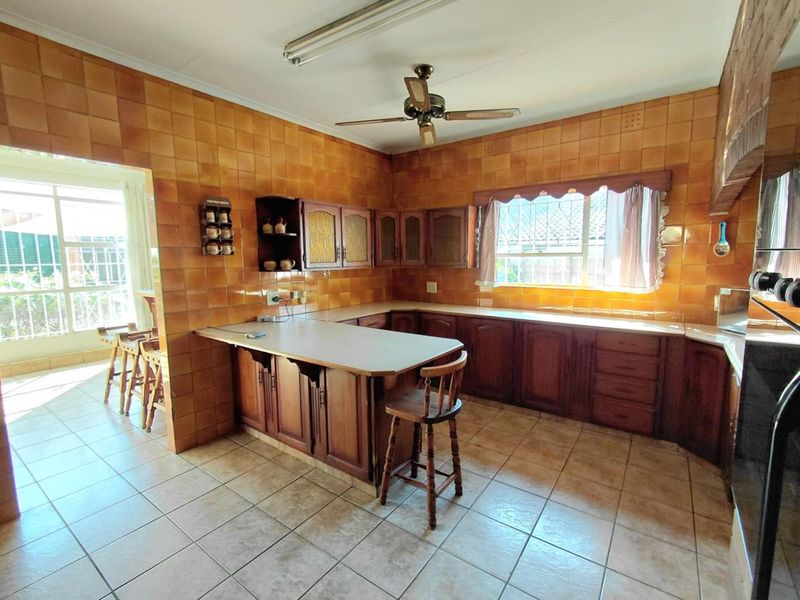 A spacious kitchen featuring extensive wooden cabinetry, a breakfast counter, and full-height ceramic wall tiling, offering a traditional layout with ample storage space.