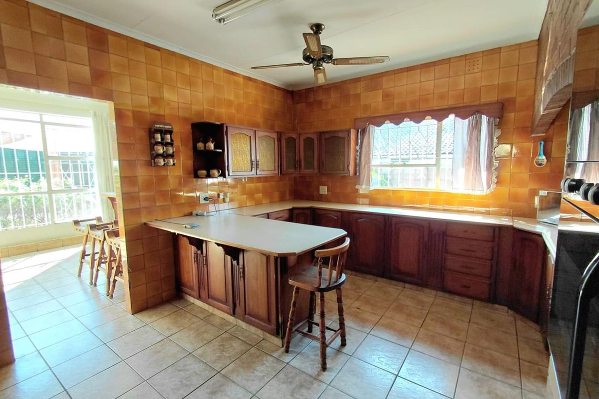 A spacious kitchen featuring extensive wooden cabinetry, a breakfast counter, and full-height ceramic wall tiling, offering a traditional layout with ample storage space.