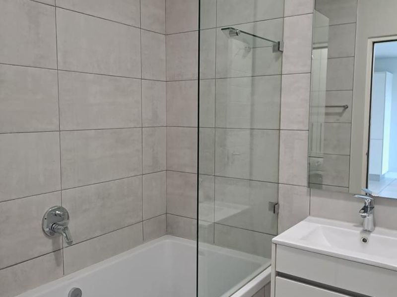 Modern bathroom featuring a built-in bathtub with a glass shower screen, wall-mounted shower head, and a sleek vanity cabinet with an integrated basin.