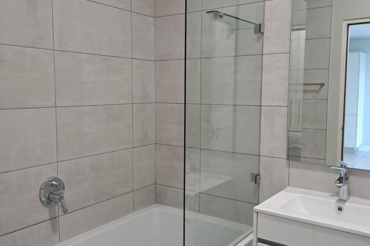 Modern bathroom featuring a built-in bathtub with a glass shower screen, wall-mounted shower head, and a sleek vanity cabinet with an integrated basin.