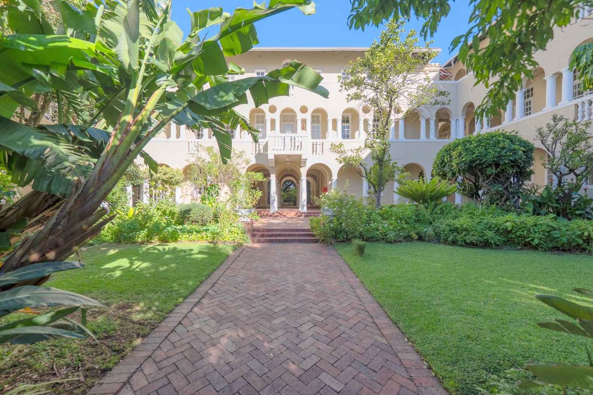 A beautifully landscaped rear garden featuring a brick paved walkway leading to an elegant building facade with arched colonnades and balconies.