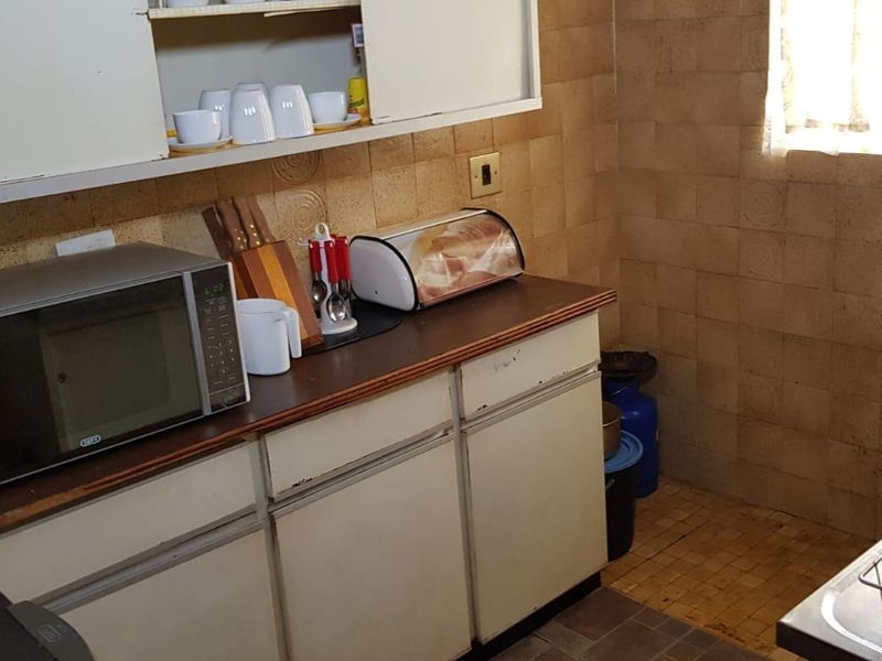A compact kitchen featuring dated cabinetry, tiled wall splashbacks, and original floor tiling, offering significant potential for a modern renovation.