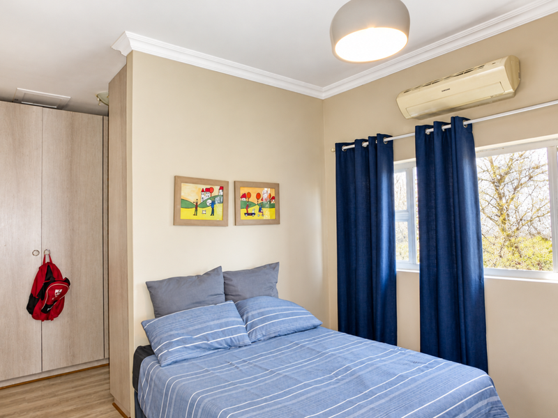 A well-maintained bedroom featuring built-in cupboards, laminate flooring, crown molding, and a wall-mounted split-system air conditioner.