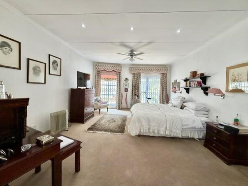 Spacious bedroom featuring neutral carpeting, recessed lighting, a ceiling fan, and sliding glass doors with security gates leading to an outdoor area.