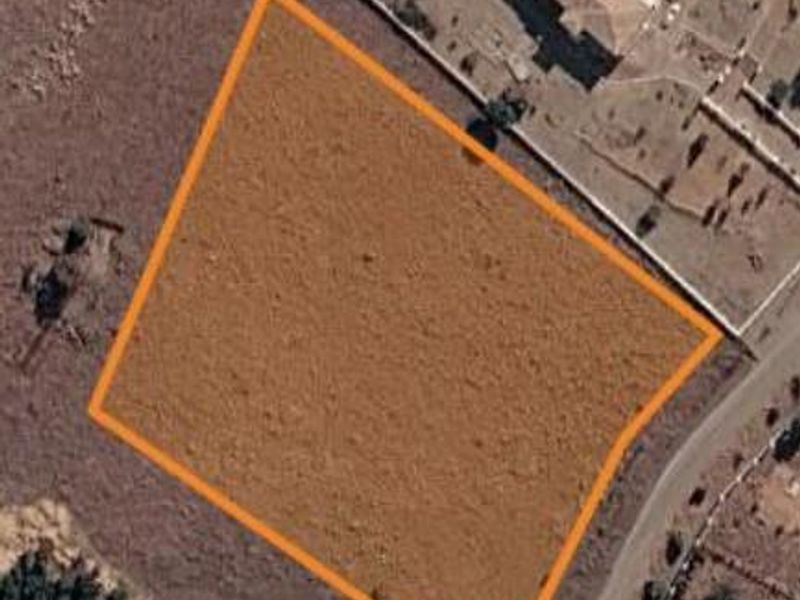 An aerial view of a vacant residential plot of land with boundary lines highlighted, situated in a developed neighborhood.