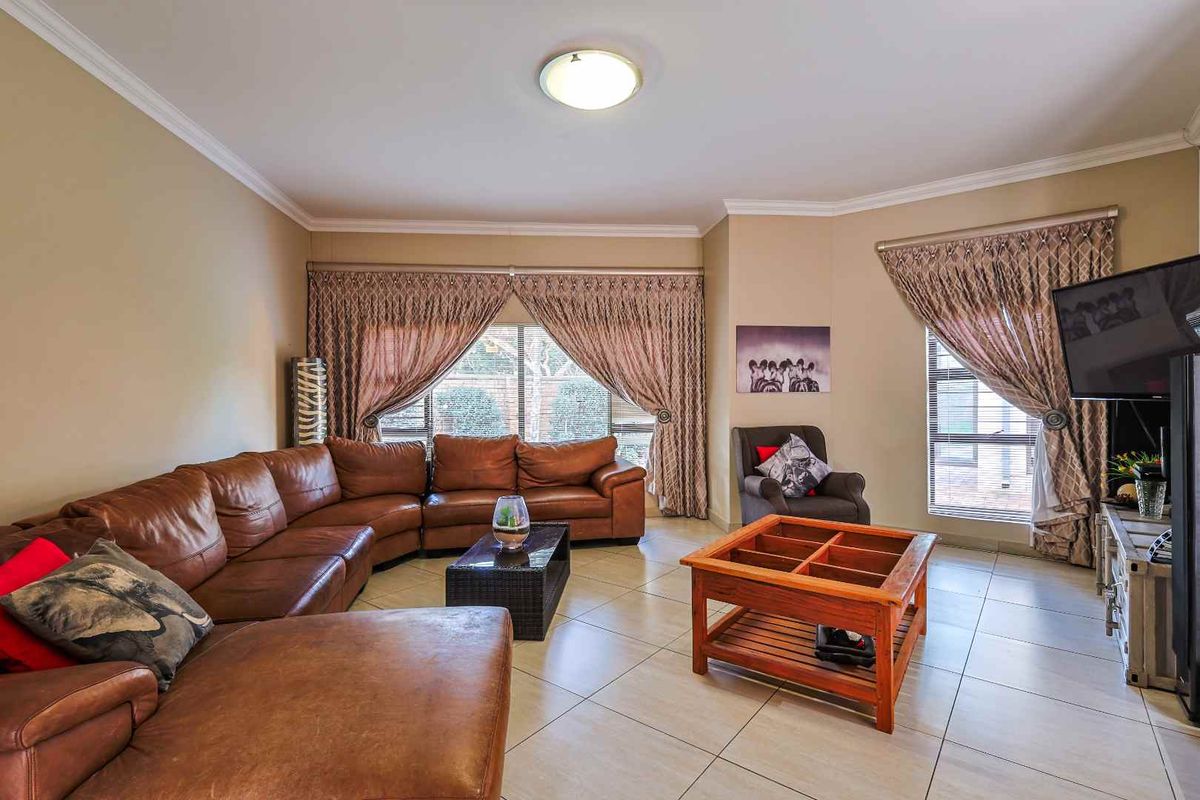 A spacious living room featuring large windows with decorative curtains and neutral tiled flooring, providing a comfortable and well-lit area for relaxation.