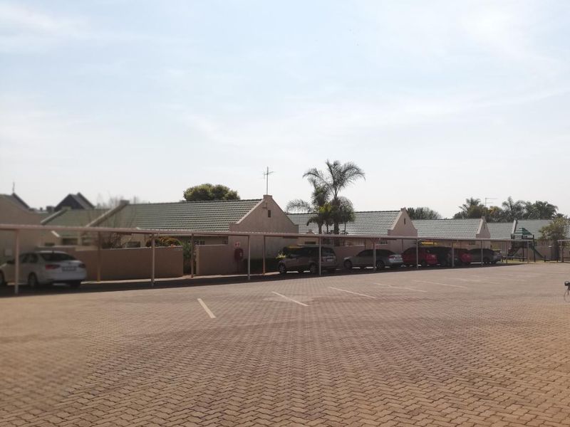 Exterior view of a townhouse complex featuring a large paved parking area with covered carports and tiled roof units.