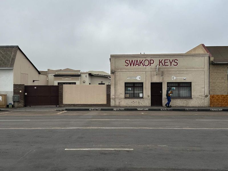 Street-facing view of a commercial property featuring a storefront with security bars and a gated entrance.