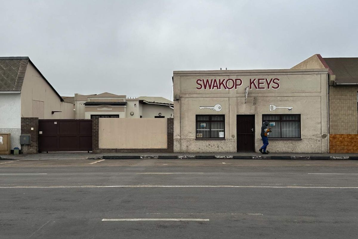 Street-facing view of a commercial property featuring a storefront with security bars and a gated entrance.