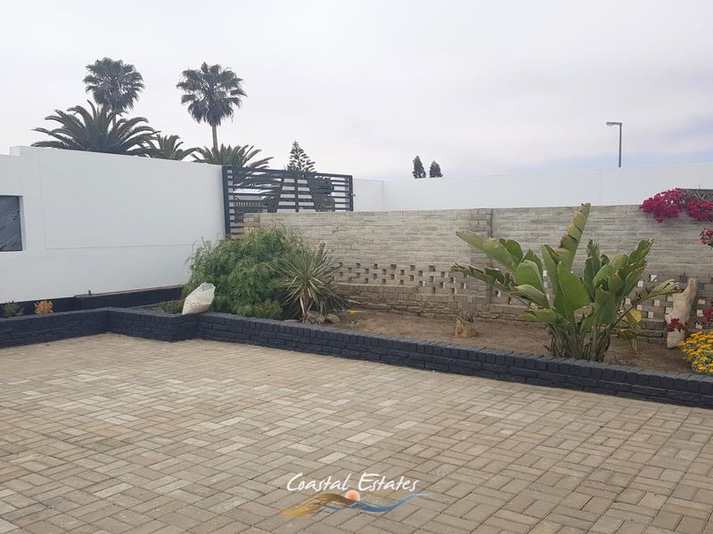 A paved rear courtyard featuring a combination of solid and decorative brick boundary walls, metal gate access, and established garden beds.