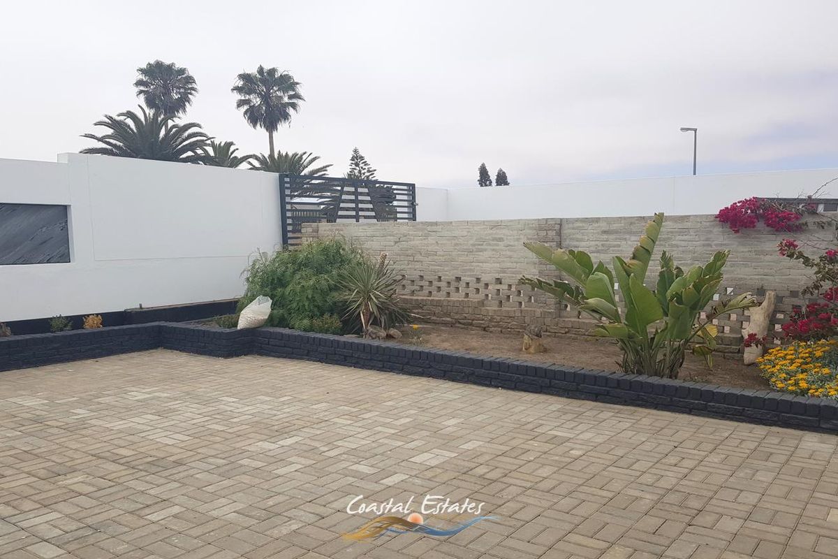A paved rear courtyard featuring a combination of solid and decorative brick boundary walls, metal gate access, and established garden beds.