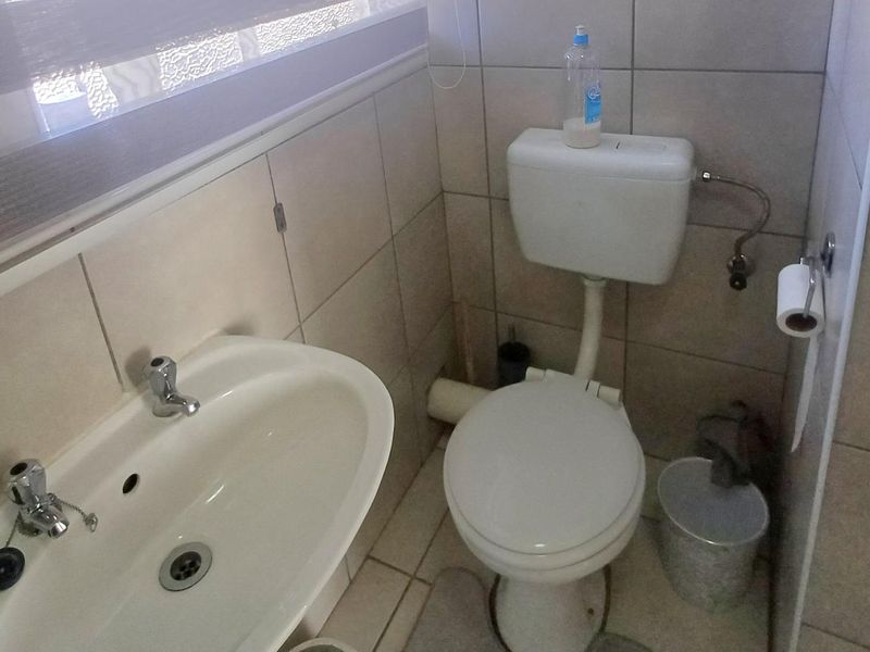 A compact bathroom featuring tiled walls and floors, a pedestal basin with chrome mixer, and a standard close-coupled toilet.