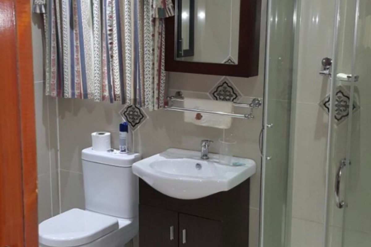A compact bathroom featuring a corner shower enclosure, a vanity basin with storage, and a standard toilet with neutral wall and floor tiling.